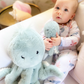 A baby in patterned pajamas sits on a white couch, holding the small Oda Octopus Plush Toy by Mon Ami—an adorable cuddle buddy—next to a larger matching plush, both perfect for baby shower gifts.