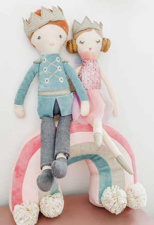 The MON AMI Prince Jean Luc Heirloom Doll, paired with a charming princess, is elegantly seated on a soft rainbow-shaped pillow by Mon Ami, creating the perfect room decor accent.