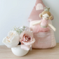 The Mon Ami Princess Castle Tooth Fairy Pillow Set is positioned next to a white vase filled with pink and white roses, creating a charming room decor setting on a wooden surface.