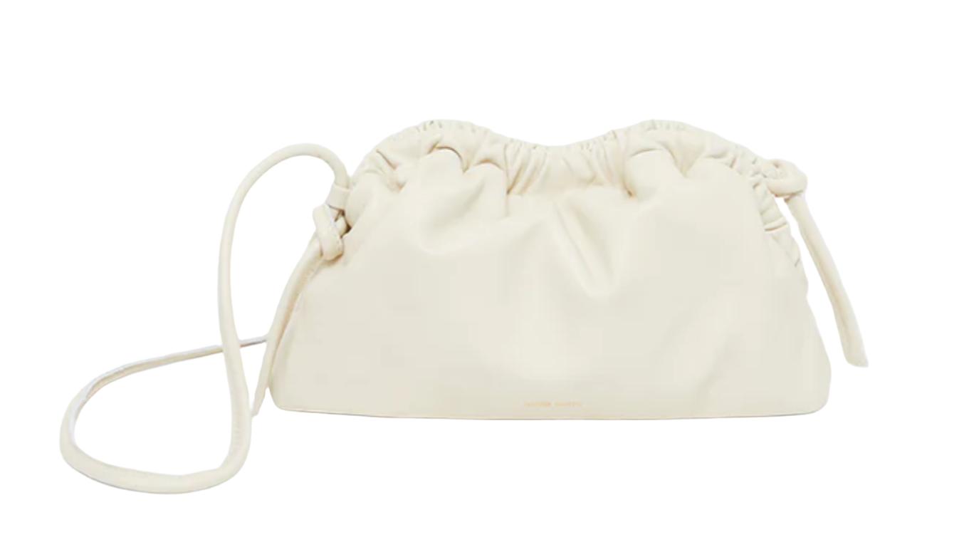 The Mansur Gavriel Mini Cloud Clutch by Mansur Gavriel is a cream-colored, ruched leather handbag crafted from exquisite Italian lamb leather, featuring a drawstring closure and a thin, multi-function removable shoulder strap. Handcrafted in Italy for unparalleled quality and style.