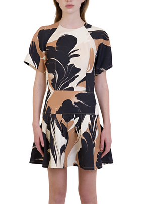 A person is wearing a Simkhai Covey Mini Dress with a black, brown, and beige abstract floral pattern. The dress features a fitted waist and pleated flared skirt with a back zipper closure.