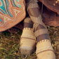 Close-up of a person's feet wearing Ulla Johnson Concha Platform Espadrille shoes with lace-up straps, standing on grass. The person is wearing a colorful, patterned dress.