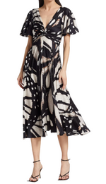 Woman wearing a knee-length Prabal Gurung Flutter Slv Twist Dress with an abstract butterfly wing pattern, V-neckline, twisted bodice, short flared sleeves, and black strappy heels.