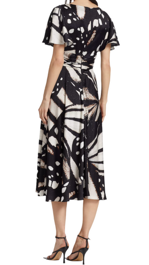 A person wearing a Prabal Gurung Flutter Slv Twist Dress in black and white abstract print with short sleeves and black high-heeled sandals is seen from the back.