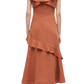 A woman wearing the 3.1 Phillip Lim Ruffle Overlay Midi Dress, featuring a rust color, shoulder frills, and an asymmetric hemline, paired with black boots, stands with her back facing the camera.