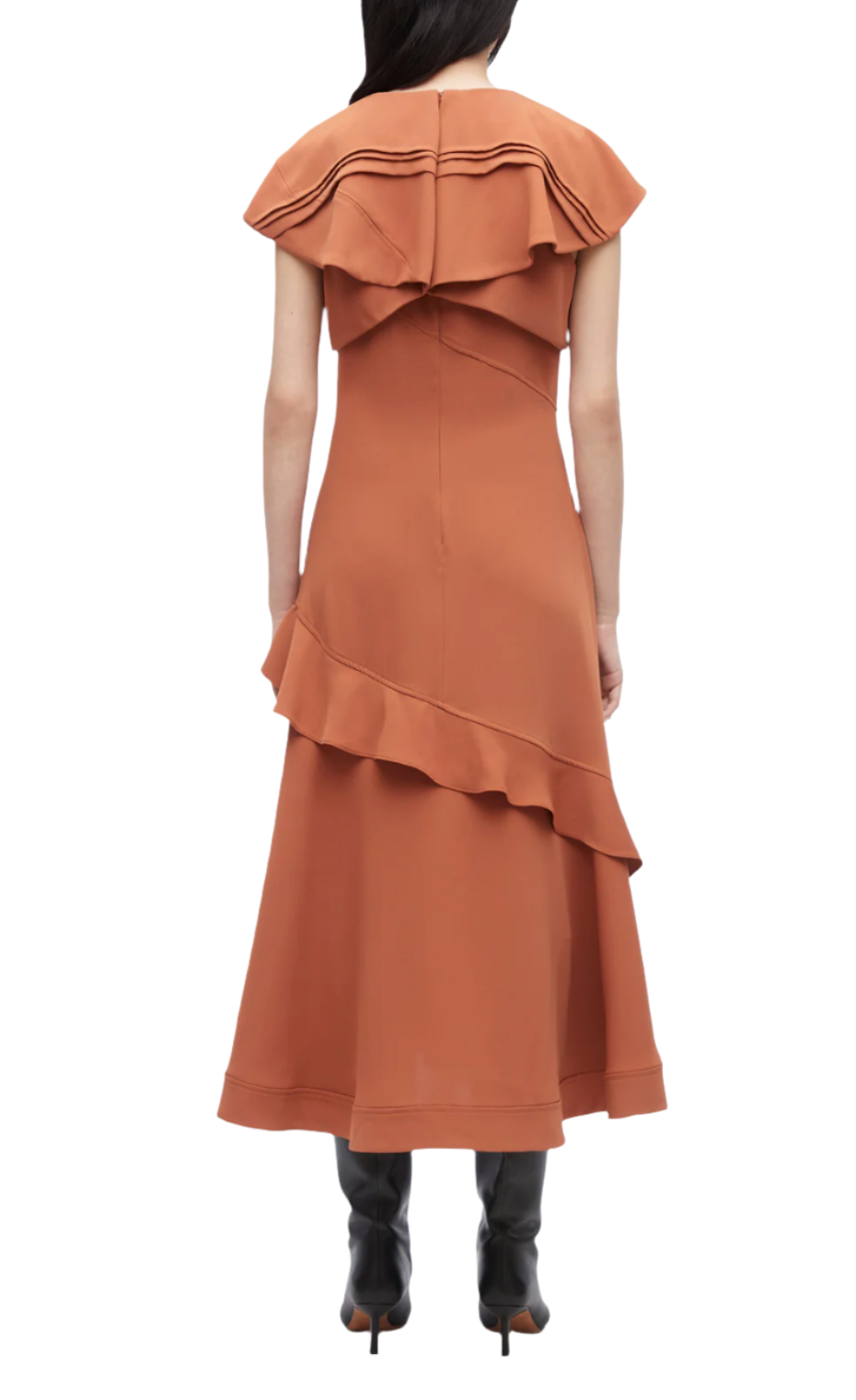 A woman wearing the 3.1 Phillip Lim Ruffle Overlay Midi Dress, featuring a rust color, shoulder frills, and an asymmetric hemline, paired with black boots, stands with her back facing the camera.