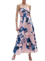 A person wearing the Figue June Dress, a pink and blue floral strapless halter-neck maxi dress with an adjustable sweetheart neckline and tiered skirt, stands against a white background.