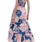 A person is wearing the Figue June Dress, a halter-neck, sleeveless piece adorned with a layered floral pattern and high heels. The dress showcases pink and blue hues and features an adjustable sweetheart neckline. The person is photographed from the back.