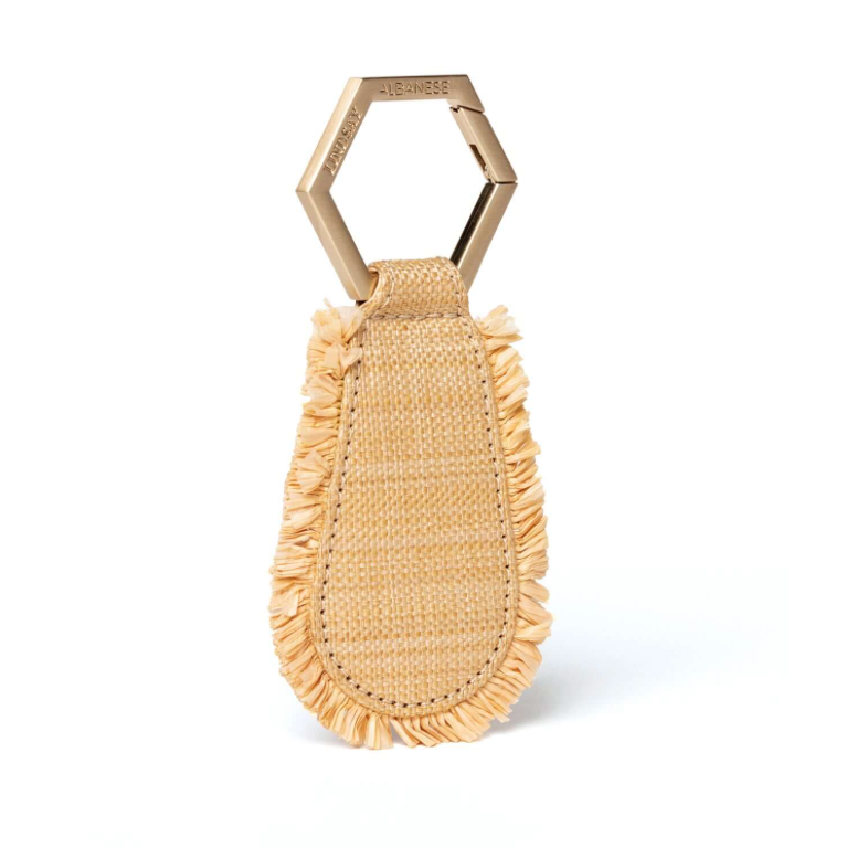 The Toptote The Fray Raffia Hat Clip by Toptote features a beige keychain with a hexagonal metal loop and fringed fabric, designed as the perfect hands-free travel solution.