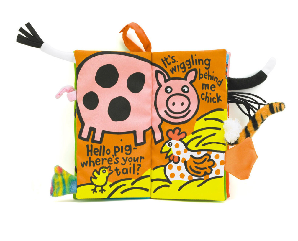 Soft fabric book for children, "Jellycat Farm Tails Book" by Jellycat, featuring a pink pig and a white chicken on a bright yellow and orange background. Text on the pages reads, "Hello pig where's your tail?" and "It's wiggling behind me chick.