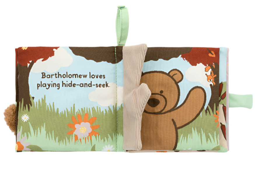 The Jellycat Bartholomew Bear Loves You Book is a soft fabric children's book. It features Bartholomew Bear playing hide-and-seek, with tactile fabrics for little hands to explore. The background showcases trees and flowers, accompanied by the text: "Bartholomew loves playing hide-and-seek.