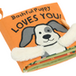 The Jellycat Bashful Puppy Loves You Book by Jellycat features an orange cloth cover adorned with a cartoon dog and the text "Bashful Puppy Loves You!" The book includes charming details such as fuzzy ears that stick out and green pages inside.