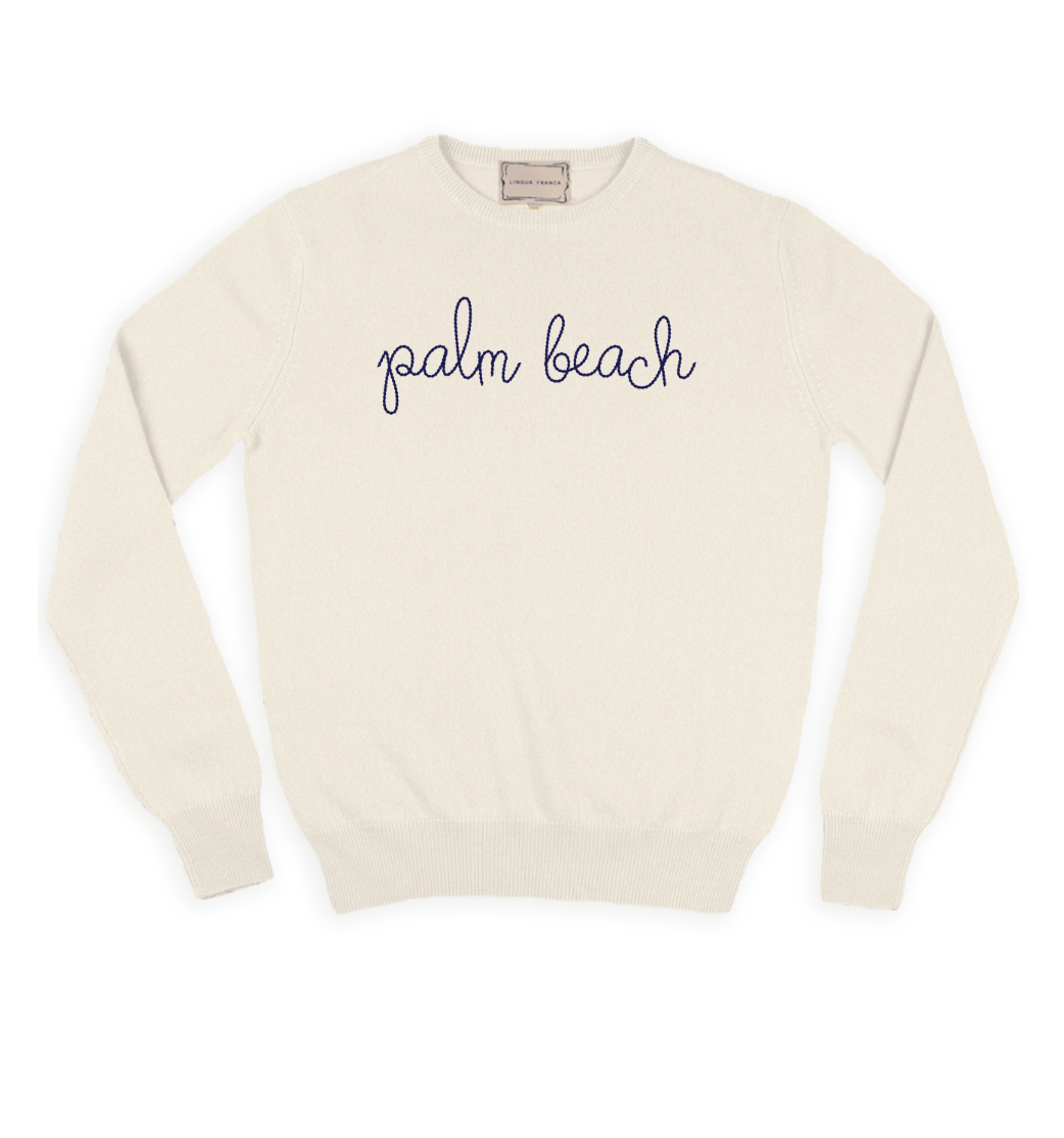 The Lingua Franca Palm Beach Classic Longsleeve Crewneck by Lingua Franca is a white cashmere sweater with long sleeves, featuring "palm beach" hand embroidered in lowercase cursive lettering on the front.