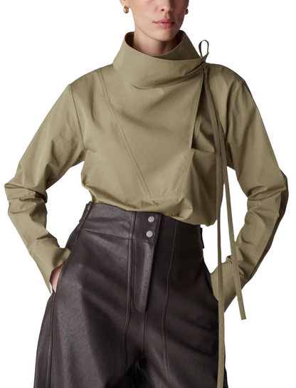 A person wearing a stylish CO Fencer's Fluid Blouse in khaki, featuring a high neck and long sleeves with an asymmetrical design, paired with high-waisted dark brown pants with a chic flyaway hem.