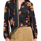 A person wearing the Dorothee Schumacher Floral Seductive Blouse, a black silk top with a flower print and a matching neck scarf, paired with light brown pants.