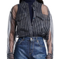 The woman wears a Dorothee Schumacher Transparent Stripe Blouse over a dark turtleneck, paired with blue jeans. The oversized silhouette from Dorothee Schumacher adds a touch of effortless style to her ensemble.