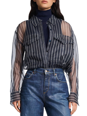 The woman wears a Dorothee Schumacher Transparent Stripe Blouse over a dark turtleneck, paired with blue jeans. The oversized silhouette from Dorothee Schumacher adds a touch of effortless style to her ensemble.