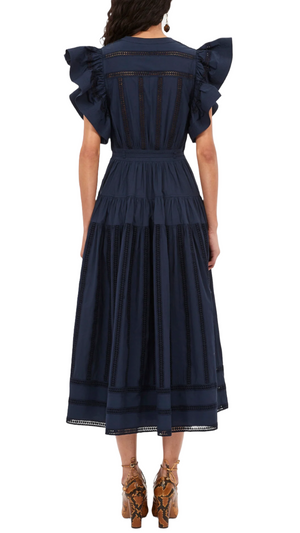 A person wearing the Ulla Johnson Emery Dress, a navy blue, knee-length outfit with ruffled sleeves and romantic detailing, viewed from the back.