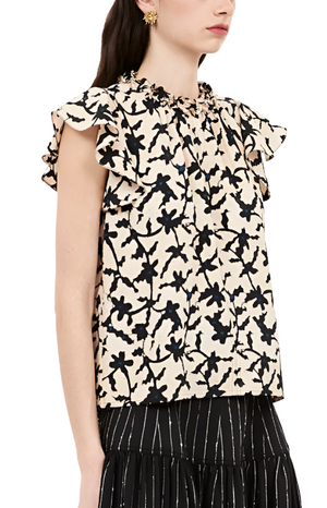 A person wears the Ulla Johnson Julia Top, a sleeveless ruffled piece featuring a black and white floral print, paired with a black skirt boasting vertical stripes.