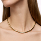 A close-up of a person wearing the elegant LIÉ STUDIO Margaret Necklace by Lie Studio, featuring elongated, tubular gold-plated brass links. The person's face is partially visible, and they have long, brown hair.