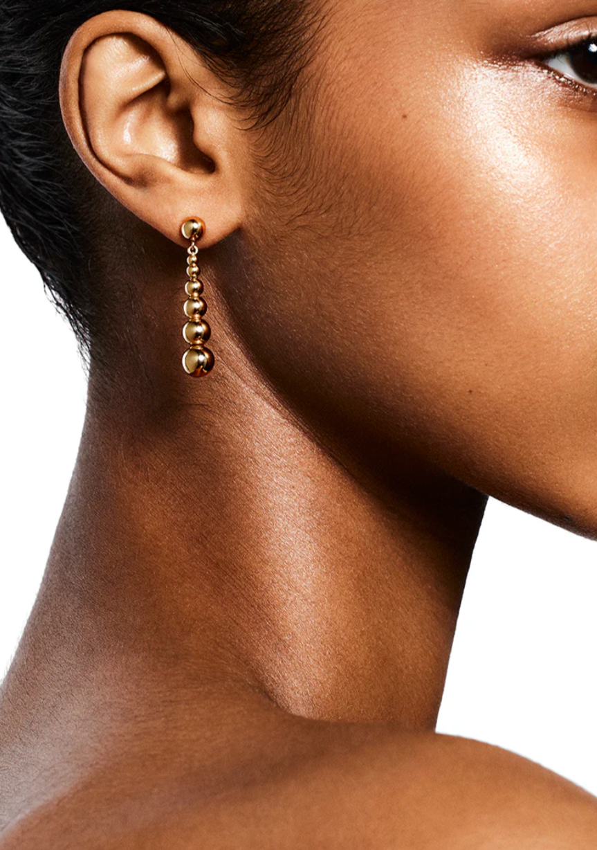 Close-up of a person wearing LIÉ STUDIO Rebecca Earrings from Lie Studio, showcasing discreet elegance with gold-plated sterling silver and a series of interconnected beads. The background is plain white.