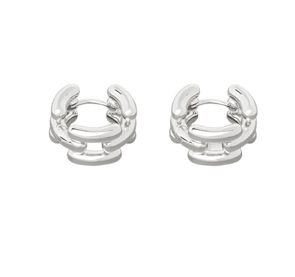 The Johanna Earrings by Lie Studio are small, silver hoops with a chunky interlocking chain design, offering elegant creol style that's perfect for everyday wear and shown on a white background.