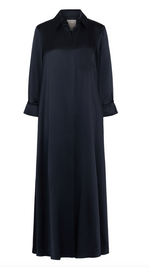 The TWP Jenny's Silk Gown from TWP is a luxurious long, navy blue maxi shirt dress with a collar and long sleeves, featuring a breast pocket and rolled cuffs, crafted from silk charmeuse for an opulent feel.