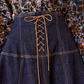 Close-up of a person wearing the Ulla Johnson The Estelle Denim Skirt with feminine lace-up detailing down the front center, paired with a patterned blouse in shades of blue, brown, and black from Ulla Johnson.