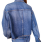 A person in an Ulla Johnson The Bobbi Denim Jacket made of rigid denim and jeans stands with their back to the camera, facing a decorative, textured wall.