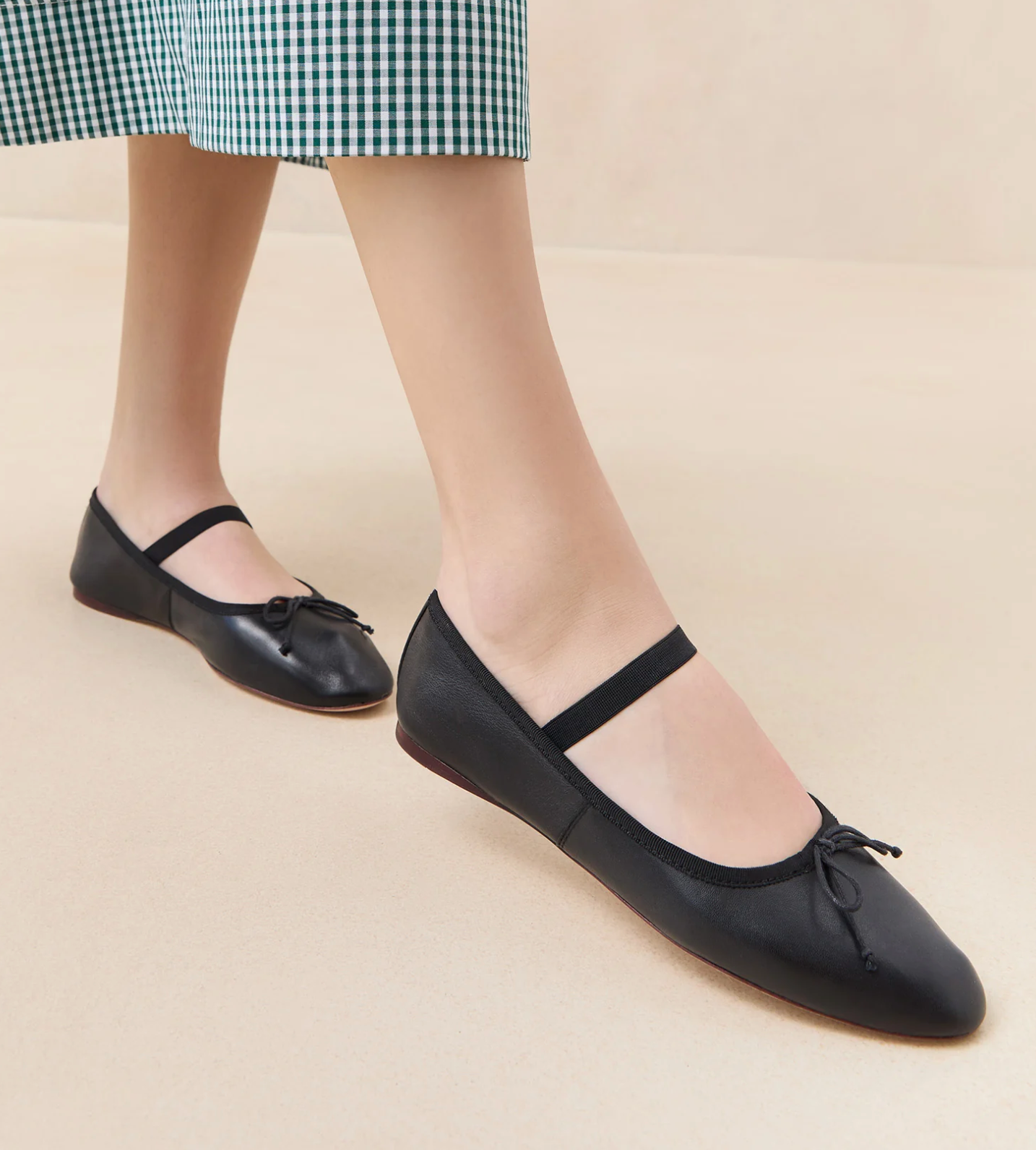 A person wearing Loeffler Randall Leonie Soft Ballet Flats, which have a strap over the instep and feature a padded footbed for added comfort. The person is also wearing a green and white checkered skirt.