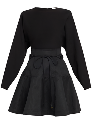 The Ulla Johnson Aremi Dress is a black long-sleeve dress with a fitted waist and a flared, layered skirt featuring a drawstring tie at the waist, offering an elegant sculptural silhouette.