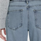 Close-up of a person wearing a gray knit sweater tucked into high-waisted, light blue Frame Slouchy Straight Wide Cuff jeans from the back. The jeans feature wide rolled cuffs and have two back pockets, with a black belt visible. Made by Frame from sustainable denim, these jeans offer a relaxed seat for ultimate comfort and style.