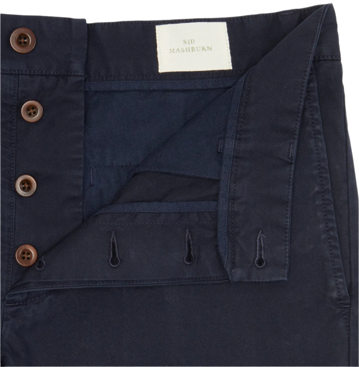 Close-up of the Sid Mashburn Garment Dyed Field Pant, slim-straight navy blue trousers made from lightweight cotton twill, featuring a button fly with brown buttons and labeled "Sid Mashburn.