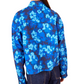 A person wearing an Ulla Johnson Aria Blouse in a vivid blue hue, paired with long sleeves and dark jeans, adorned with eye-catching ikat floral patterns, viewed from the back.