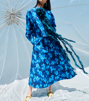 Beneath a white canopy, someone stands wearing the Ulla Johnson Vianne Skirt in a blue ikat floral design, featuring large ruffle details.