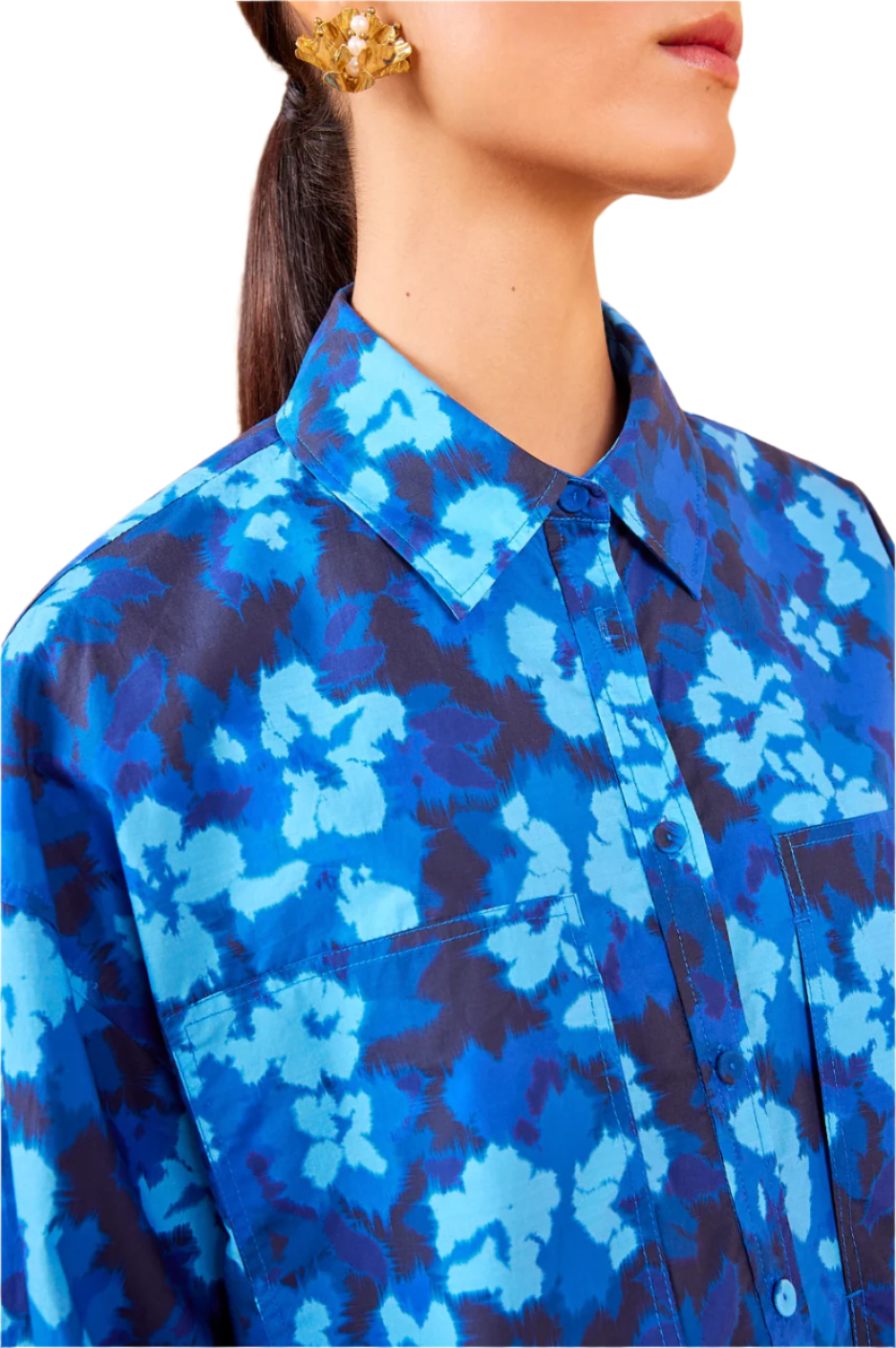 Close-up of a person wearing the Ulla Johnson Aria Blouse, highlighting its blue ikat floral pattern paired with gold earrings.