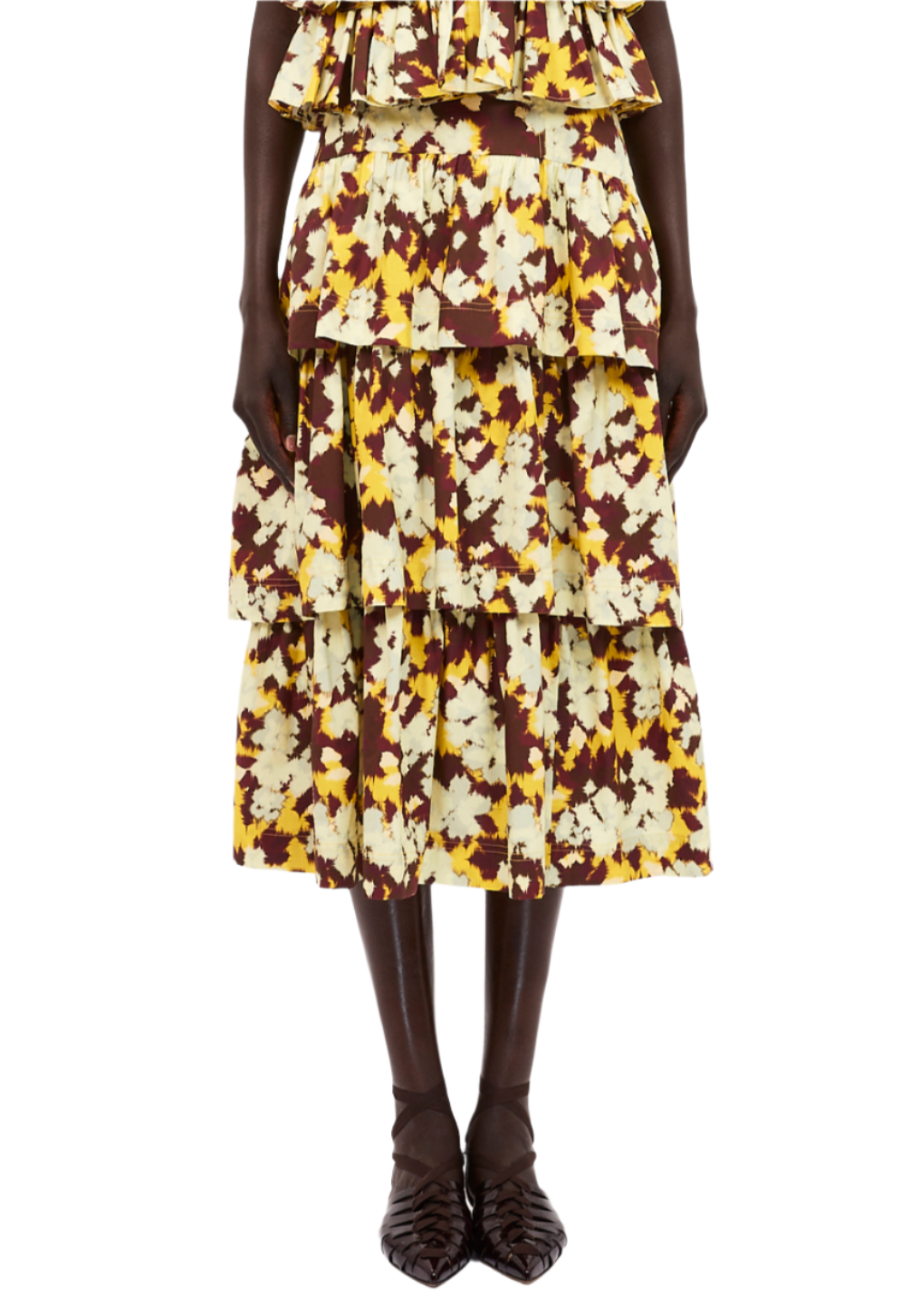 A person wearing the Ulla Johnson Winnie Skirt, a midi-length, multi-tiered skirt with yellow and brown floral patterns featuring ruffled tiers, paired with dark pointed shoes.