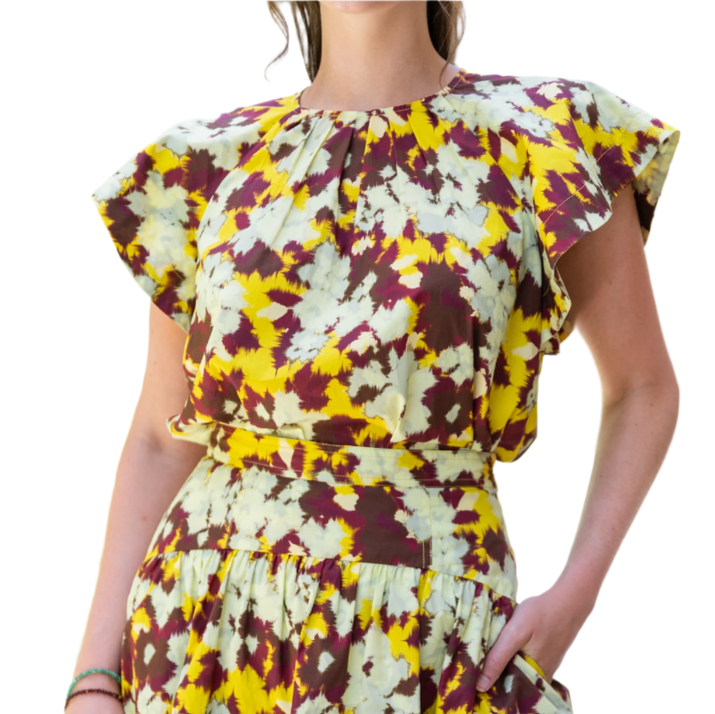 A person is wearing the Ulla Johnson Rumi Top, showcasing a vibrant pattern in yellow, purple, and cream with flutter sleeves and pockets, reminiscent of ikat florals.