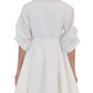 Rear view of a person wearing the Simkhai Jazzie Mini Dress, a white, short, flared poplin dress with rolled-up sleeves, set against a white background.