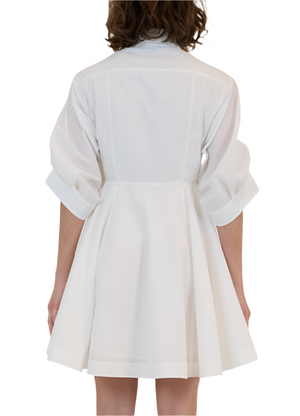 Rear view of a person wearing the Simkhai Jazzie Mini Dress, a white, short, flared poplin dress with rolled-up sleeves, set against a white background.