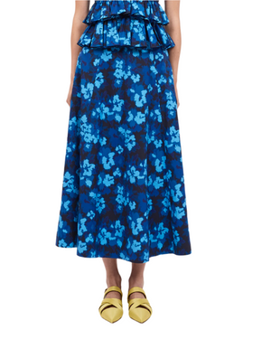 A person is elegantly dressed in an Ulla Johnson Vianne Skirt in a blue ikat floral pattern, paired with bright yellow pointed shoes.