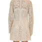 A person stands with their back to the camera wearing a Simkhai Charis Mini Dress in cream, featuring long sleeves and embroidered eyelet details in a wavy pattern.