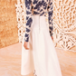 A person wearing the Ulla Johnson Brigette Skirt, a white high-waisted A-line design, paired with a blue floral long-sleeve top, stands elegantly in front of a decorative textured wall.