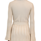 A person with shoulder-length hair faces away, wearing the Simkhai Aris Top in light beige. The top features elegant flared sleeves and a pleated design.