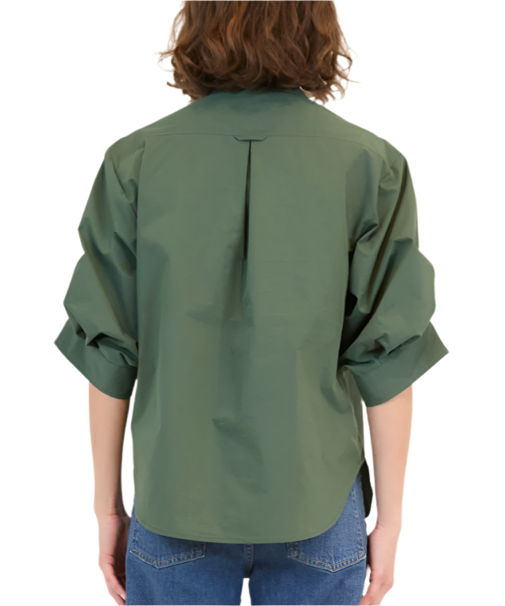 A person wearing a Simkhai Gemma Shirt, a tailored fit green button-up with rolled-up sleeves and a classic collar, paired with blue jeans, is viewed from the back.