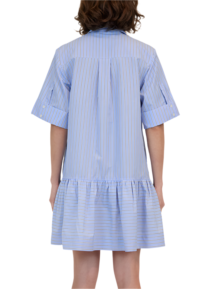 A person is wearing the Simkhai Cris Shirt Dress, characterized by its loose fit and blue and white stripes, with a button-down front and traditional collar, featuring a ruffled hem, viewed from the back.