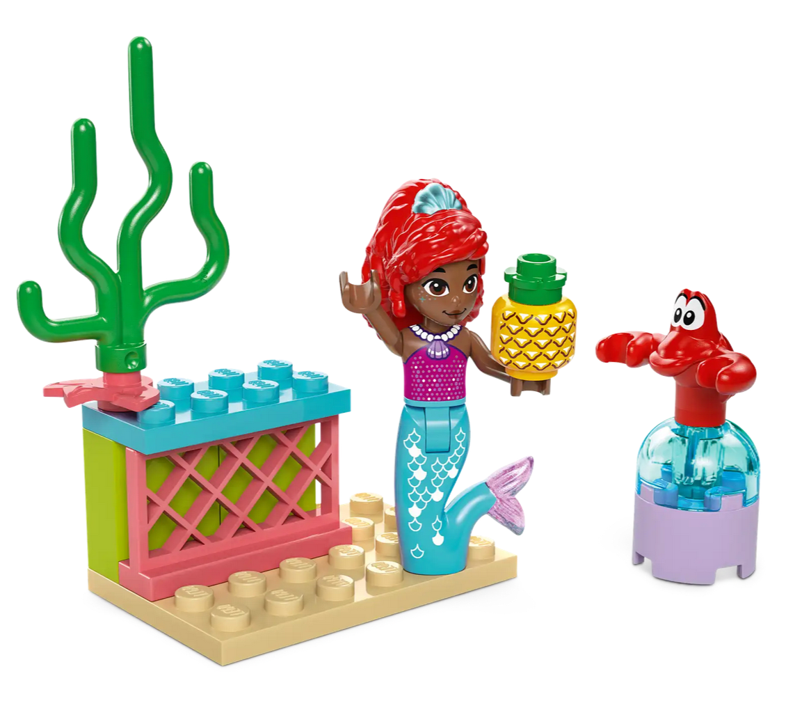 A LEGO® Disney Ariel's Music Stage set from Legos - Toyhouse features a mermaid figure that resembles Disney’s Ariel, holding a pineapple next to a red crab figure and a piece of coral. The enchanting scene is completed with a small structure crafted from colorful building blocks.