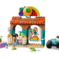 A lively scene at the LEGO® Friends Beach Smoothie Stand from Legos - Toyhouse features play food sets accompanied by two figures, a compact vehicle, and a palm tree. The decorative stand is topped with an eye-catching large fruit sign, and in the foreground, a small green crab-like toy adds charm. This set is perfect for LEGO Friends enthusiasts!