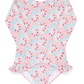 The Minnow Girls' Rashguard One Piece is a long-sleeve pink swimsuit that showcases a charming floral and dolphin print. It features sun-safe fabric and ruffled details at the hips for an added touch of style.