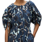 A person is wearing the 3.1 Phillip Lim Abstract Vines Belted Dress, which features a blue, black, and white pattern with abstract vines, puff sleeves, a cinched waist, and a tiered skirt.